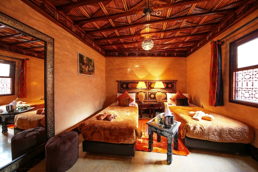 Riad Africa Marrakech twin beds room with ornate wooden ceiling, warm ochre walls, patterned bedspreads, and decorative cushions