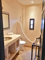 Bathroom in Riad Bouchedor in Ouarzazate featuring beige plaster walls, a built-in sink, traditional tiles, and a small window