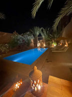 Riad Bouchedor in Ouarzazate featuring a lit outdoor pool at night with lanterns and palm trees around the courtyard