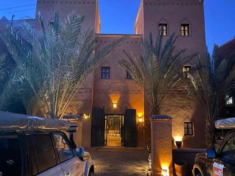 Riad Bouchedor in Ouarzazate showing traditional Moroccan mud brick architecture with ornate wooden doors and palm trees at dusk