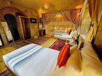 Riad Chay Boutique warm-toned bedroom with twin beds, colorful patterned rugs, textured walls, and sheer curtains