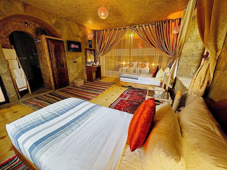 Riad Chay Boutique warm-toned bedroom with twin beds, colorful patterned rugs, textured walls, and sheer curtains