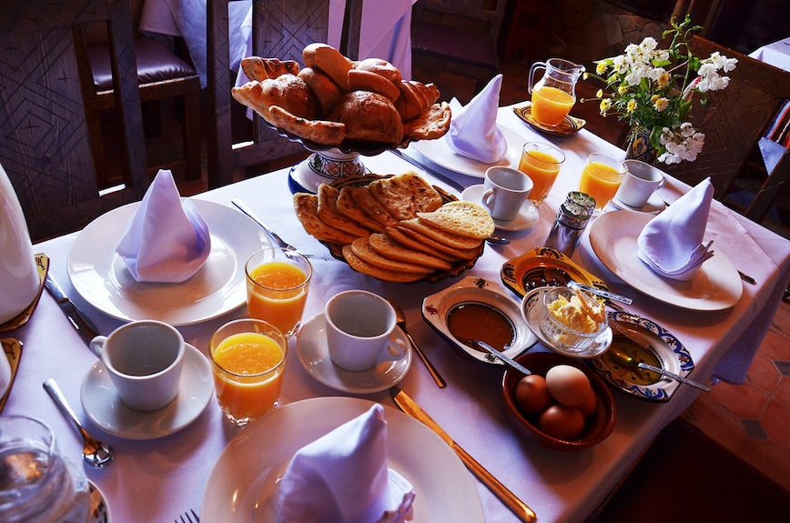 Riad Chay Boutique breakfast table with fresh bread, orange juice, eggs, and white napkins on a white tablecloth