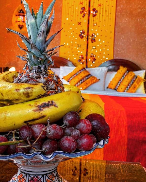 Riad Chay Boutique fruit bowl with bananas, pineapple, and grapes in bright Moroccan-style room with orange and yellow decor