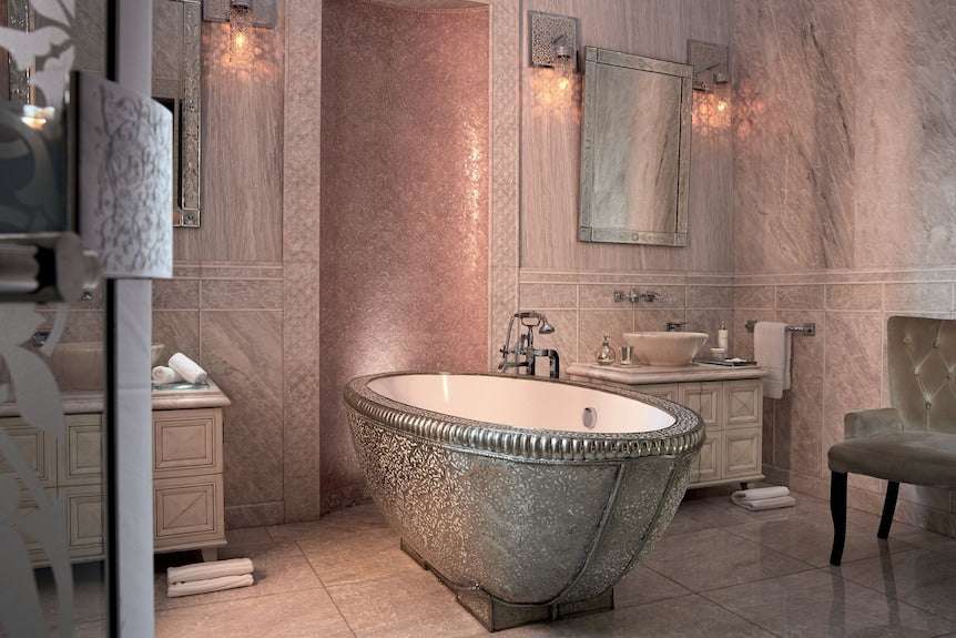 Riad Chay Boutique elegant bathroom with metallic silver freestanding bathtub, marble walls, decorative mirrors, and plush beige chair