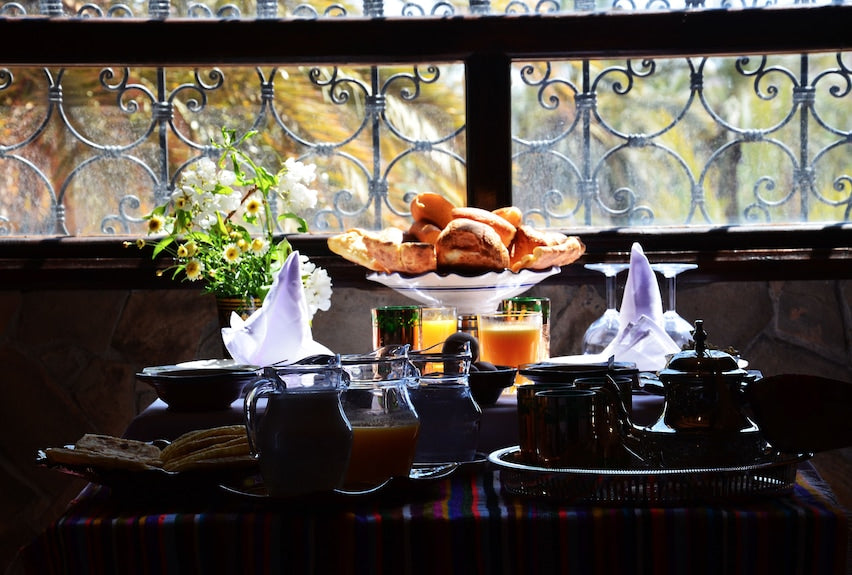 Riad Chay Boutique traditional Moroccan breakfast setup with fresh bread, orange juice, tea set, and flowers on a patterned tablecloth