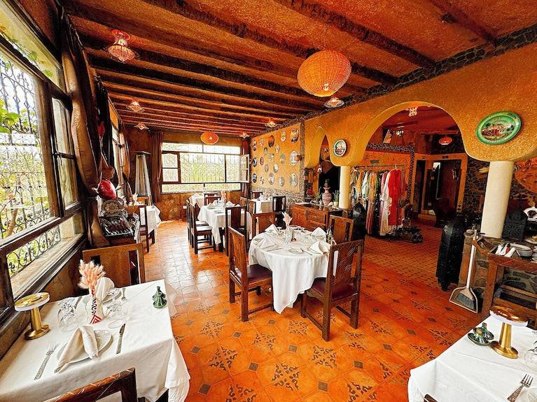 Riad Chay Boutique Moroccan dining room with warm orange tones, wooden beams, patterned tile floor, and white tablecloths