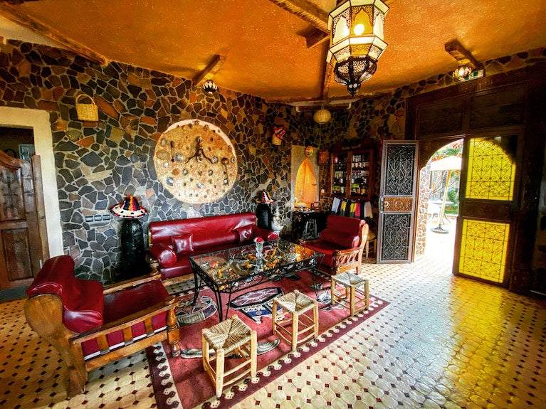 Riad Chay Boutique Moroccan living room with red leather seating, ornate mosaic tile floor, stone accent wall, and traditional lantern lighting