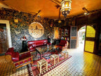 Riad Chay Boutique Moroccan living room with red leather seating, ornate mosaic tile floor, stone accent wall, and traditional lantern lighting