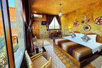 Riad Chay Boutique Moroccan-style bedroom with stone walls, wooden bed with striped brown bedding, woven chairs, and decorative wall hangings