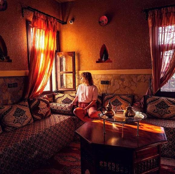 Riad Chay Boutique Moroccan-style room with warm orange walls, patterned cushions, traditional textiles, and a wooden tea table