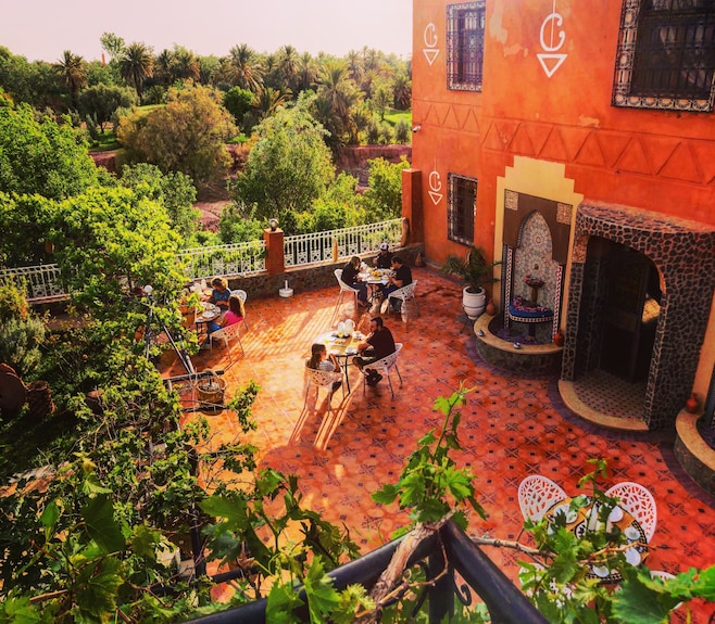 Riad Chay Boutique outdoor terrace with terracotta tile flooring, Moroccan decorative wall fountain, and guests dining at black metal tables