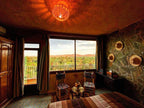 Riad Chay Boutique room with earth-toned decor, patterned tiled floor, wooden furniture, and large window overlooking lush greenery and distant hills