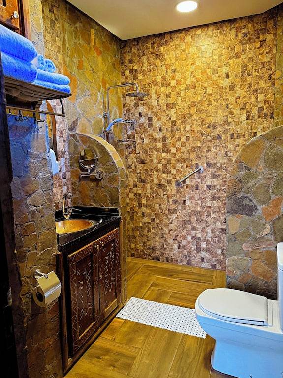 Riad Chay Boutique rustic bathroom with mosaic stone walls, carved wooden vanity, copper sink, and white toilet