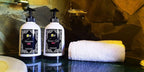 Riad Chay Boutique branded white shampoo and rose shower gel bottles with black pump tops alongside a rolled white towel on a stone countertop