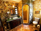 Bathroom with stone-textured walls, tiled floor, wooden vanity with green countertop, and arched shower space in Riad Chay Boutique