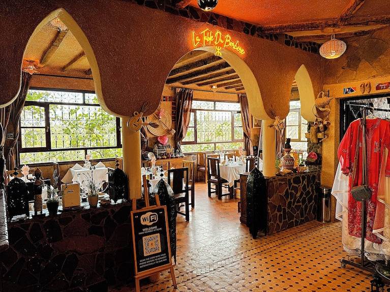 Riad Chay Boutique interior featuring warm orange tones, traditional Moroccan arches, tiled floors, and decorated dining area with tables and chairs