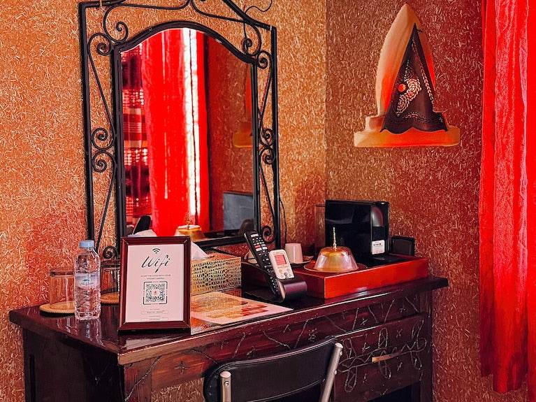 Riad Chay Boutique wooden dressing table with ornate mirror, red textured walls, decorative lamp, and red curtains