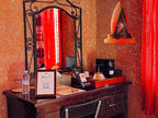 Riad Chay Boutique wooden dressing table with ornate mirror, red textured walls, decorative lamp, and red curtains