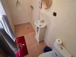 Bathroom in Riad Dar Menorca with white fixtures, beige tiled floor, round mirror, and red floor mat