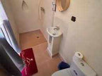 Bathroom in Riad Dar Menorca with white fixtures, beige tiled floor, round mirror, and red floor mat