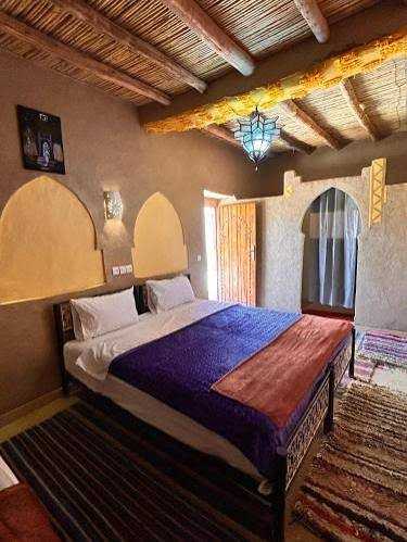 Riad Dar Menorca bedroom with rustic wooden ceiling, brown walls, double bed with purple and orange blankets, and arched wall niches