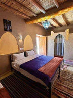 Riad Dar Menorca bedroom with rustic wooden ceiling, brown walls, double bed with purple and orange blankets, and arched wall niches