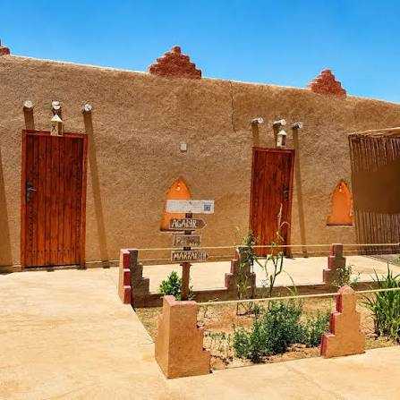 Riad Dar Menorca exterior wall in Merzouga Morocco with sandy brown adobe texture and wooden doors under clear blue sky