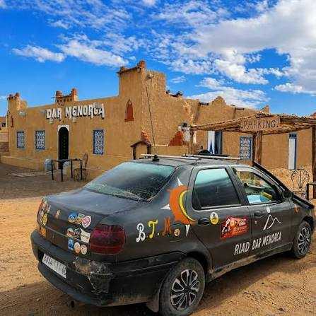 Riad Dar Menorca with traditional beige adobe walls and blue tile accents beside a black car with colorful stickers and signage on doors