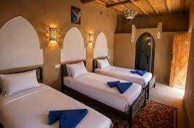 Riad Dar Menorca room with three single beds, beige textured walls, wooden ceiling, and blue towels on beds