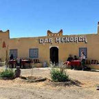 Riad Dar Menorca traditional beige mud brick building with a tiled roof, Moroccan style windows, and outdoor seating area with cushions