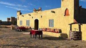 Riad Dar Menorca exterior in warm yellow with traditional Moroccan tiles and red cushions under clear blue sky