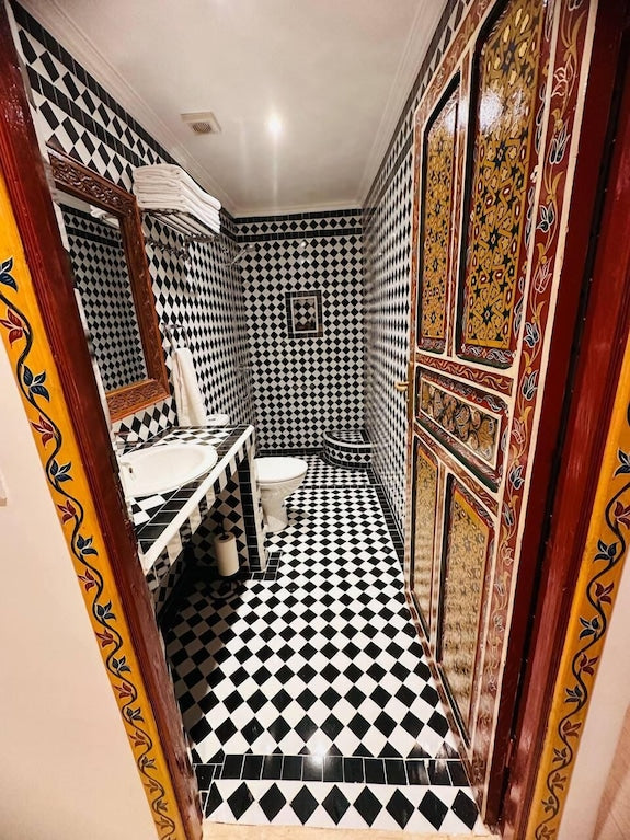 Bathroom at Riad Dar Tahri SPA featuring black and white diamond-patterned tiles with traditional Moroccan decorative wood door and mirror frame