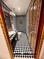 Bathroom at Riad Dar Tahri SPA featuring black and white diamond-patterned tiles with traditional Moroccan decorative wood door and mirror frame