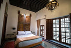 Riad Dar Tahri SPA bedroom featuring a large wooden carved headboard, white bedding, beige throw, patterned tile floor, and ornate ceiling lantern