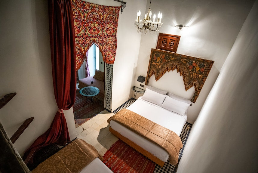 Riad Dar Tahri SPA bedroom with white walls, patterned colorful textile decor, red curtains, and traditional Moroccan furnishings