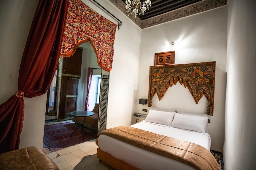 Bedroom at Riad Dar Tahri SPA featuring white walls, traditional Moroccan tapestry, brown bedspread, and decorative wooden ceiling