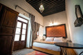 Riad Dar Tahri SPA bedroom with a wooden framed double bed, white linens, orange patterned headboard, patterned curtains, and tiled floor