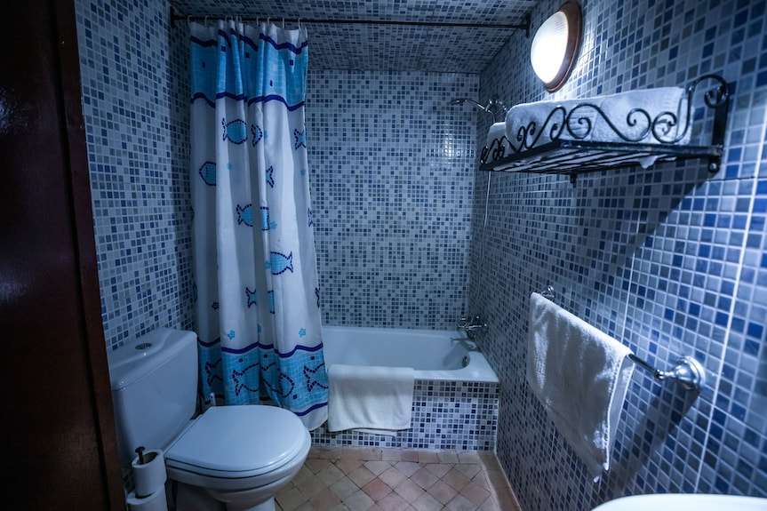 Bathroom in Riad Dar Tahri SPA featuring blue mosaic tiled walls, white bathtub with fish-patterned shower curtain, toilet, and towels
