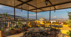 Riad Dar Tahri SPA covered terrace with black wrought iron tables and chairs and yellow cushioned benches overlooking scenic hills