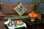 Riad Dar Tahri SPA cozy seating with patterned cushions, traditional Moroccan textiles, teapot, mint tea, pastries, and oranges
