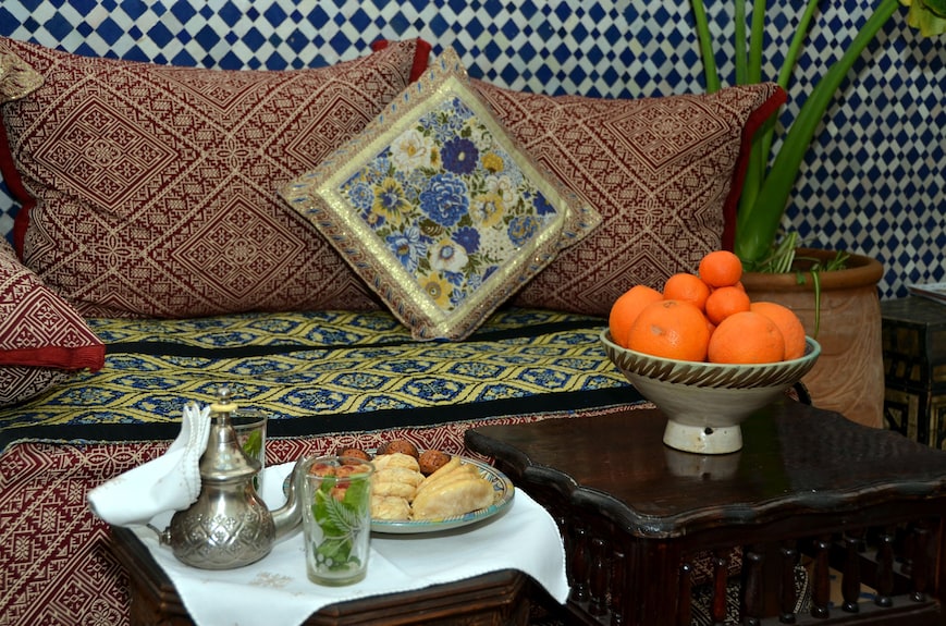 Riad Dar Tahri SPA cozy seating with patterned cushions, traditional Moroccan textiles, teapot, mint tea, pastries, and oranges