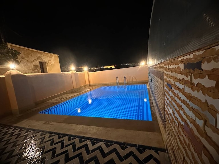 Outdoor illuminated swimming pool with blue water and mosaic tile patterns at night in Riad Dar Tahri SPA