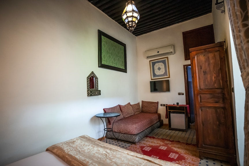 Traditional Moroccan bedroom at Riad Dar Tahri SPA featuring wooden ceiling, patterned cushions, rustic wardrobe, and vibrant rug