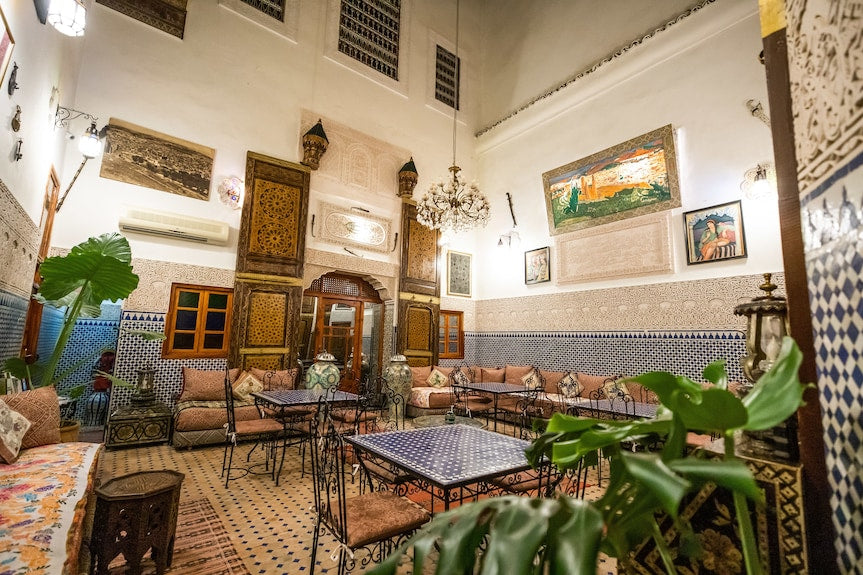 Riad Dar Tahri SPA lounge with traditional Moroccan tiled walls, patterned floor, intricate wooden doors, and iron furniture with cushions