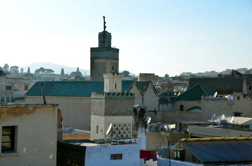 Traditional Moroccan riad buildings with beige walls and green tiled rooftops in historic Fes medina during daytime near Riad Dar Tahri SPA