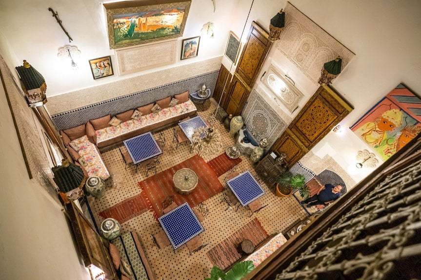 Riad Dar Tahri SPA traditional Moroccan seating area with patterned cushions, mosaic tables, decorative rugs, and wall art