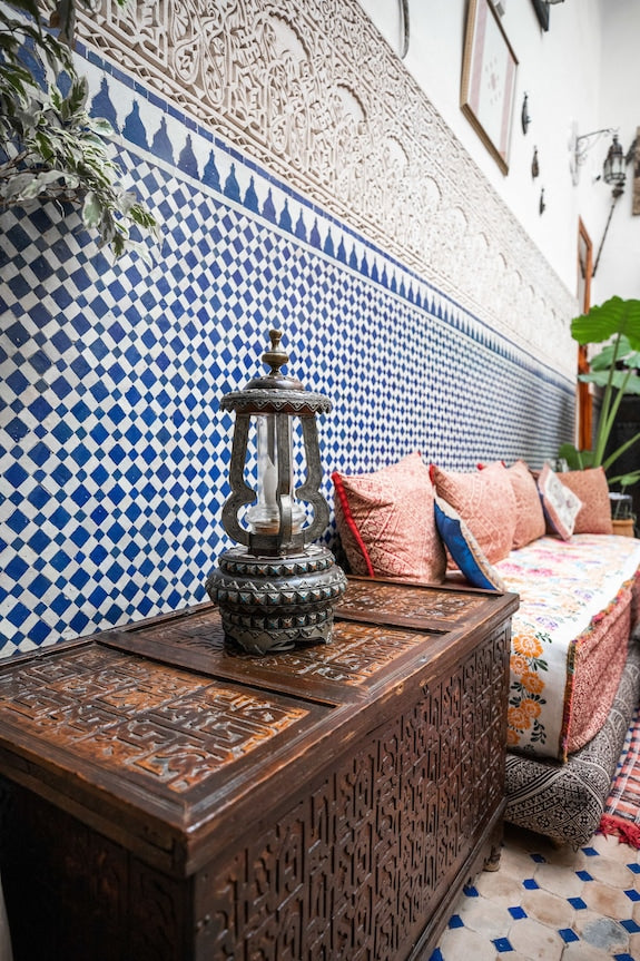 Riad Dar Tahri SPA blue and white tiled wall with intricate wooden chest topped by a decorative lantern and traditional Moroccan cushions