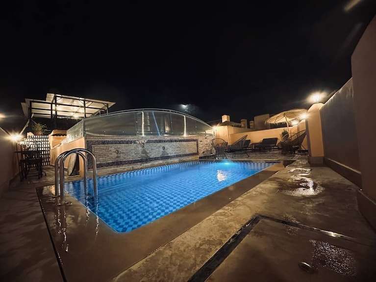 Riad Dar Tahri SPA outdoor swimming pool lit at night with tiled interior and surrounding lounge chairs