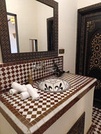 Riad La Luna decorative bathroom sink with brown and white tiled countertop, ornate mirror frame, and black patterned door
